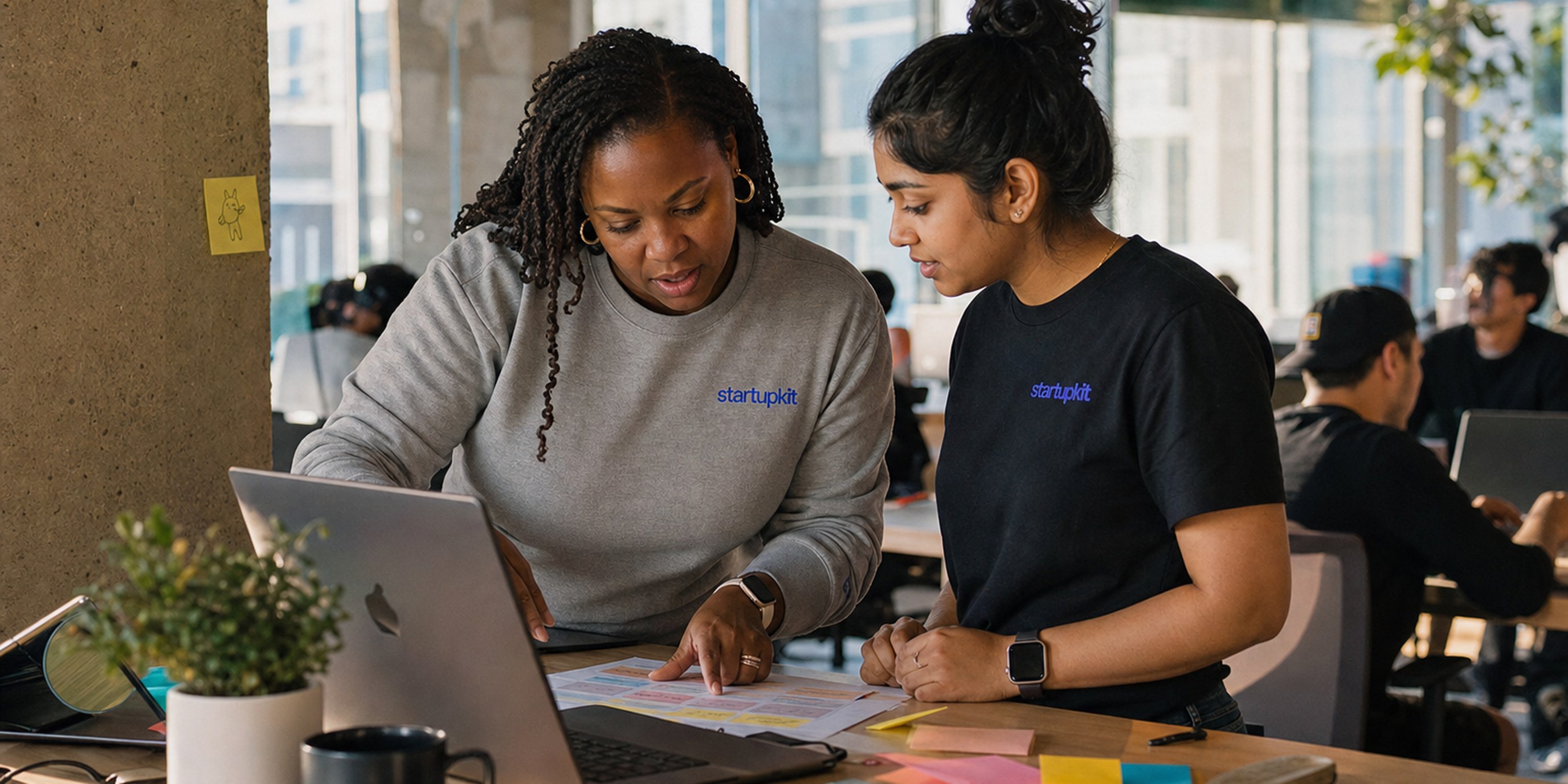 Two security program owners reviewing a severity-tiered bounty matrix and resolution SLA on a laptop in a sunlit San Francisco co-working space