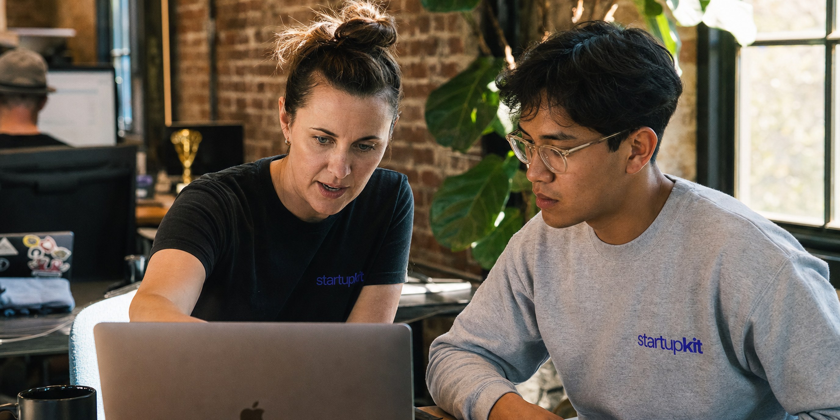 Founder reviewing an AI-assisted hiring dashboard with a colleague in a sunlit startup loft
