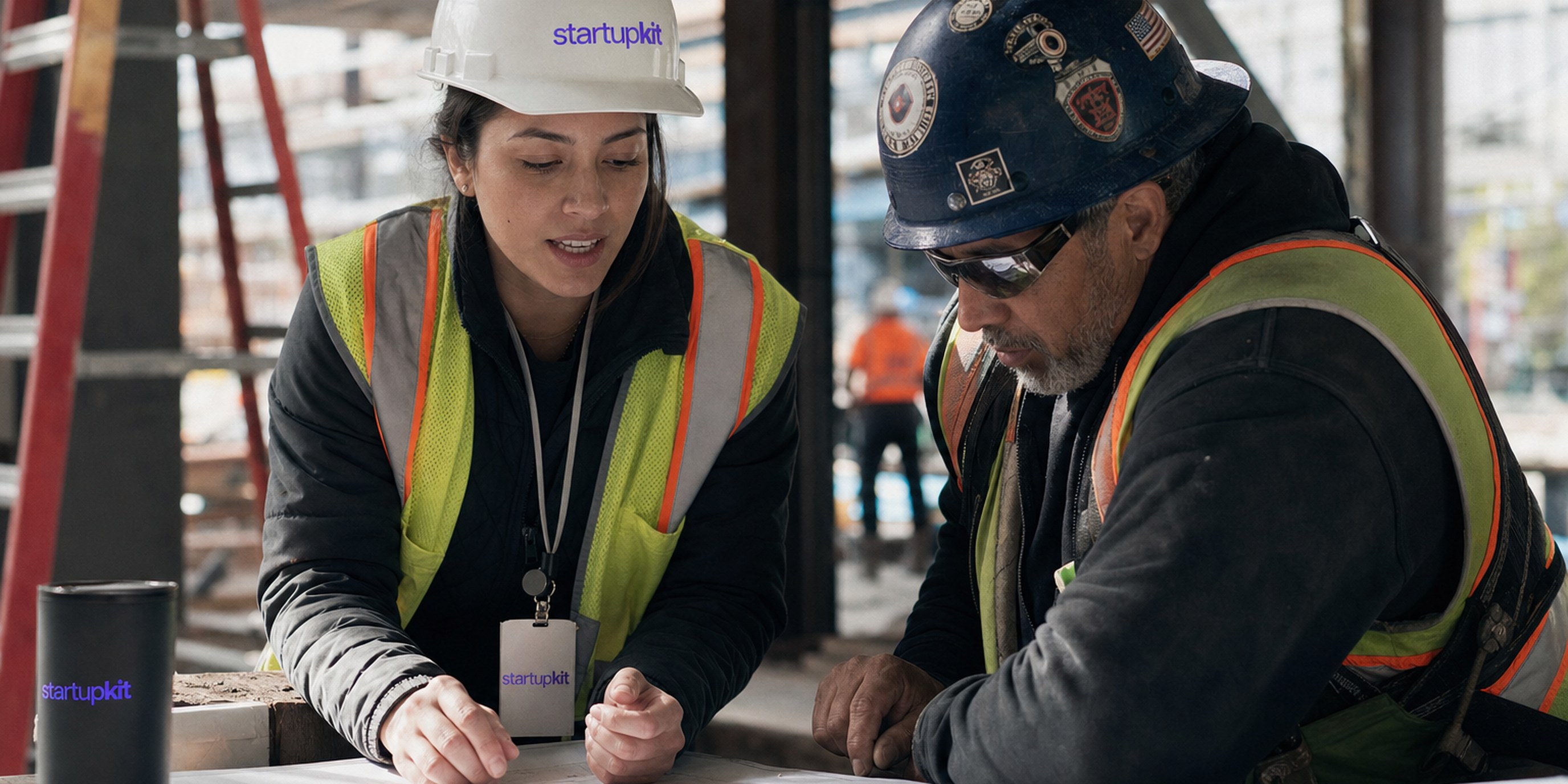 Construction project manager in a hard hat and safety vest reviewing schedule drawings with a superintendent at an active jobsite