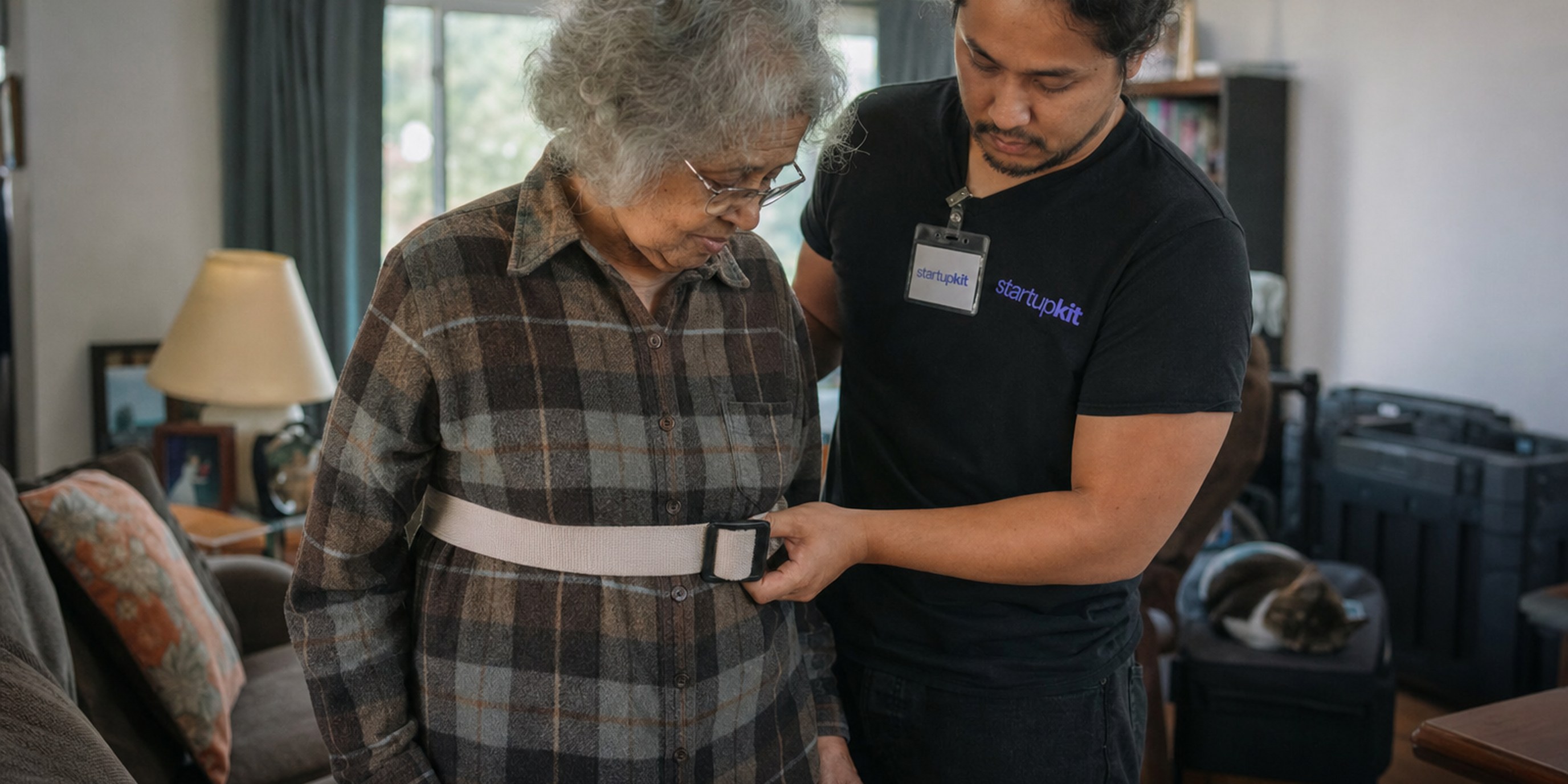 A home health aide using a gait belt to help an older woman walk across her living room