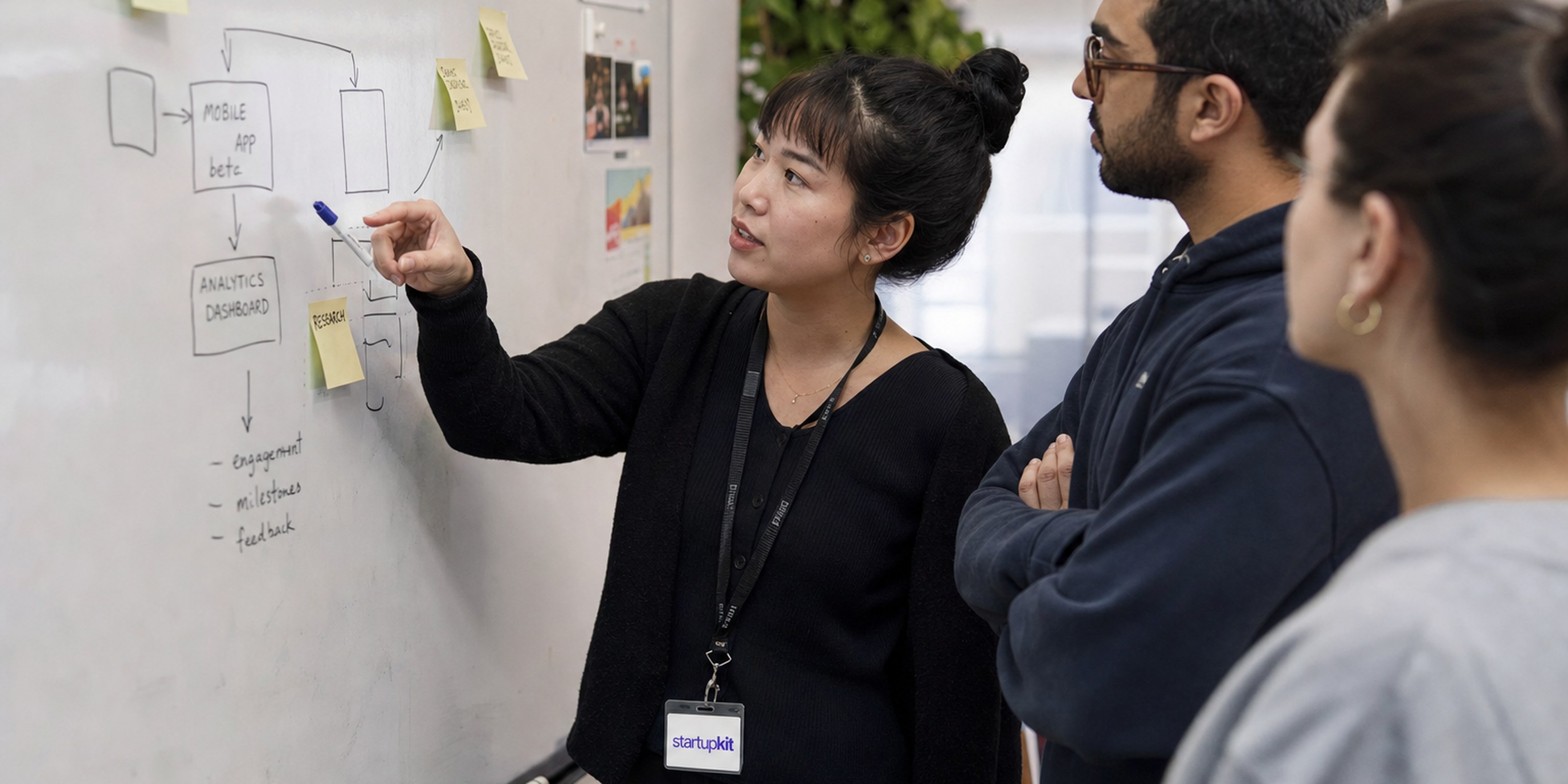 A product manager leading a product roadmap discussion at a whiteboard with two startup engineers, illustrating how to hire a product manager
