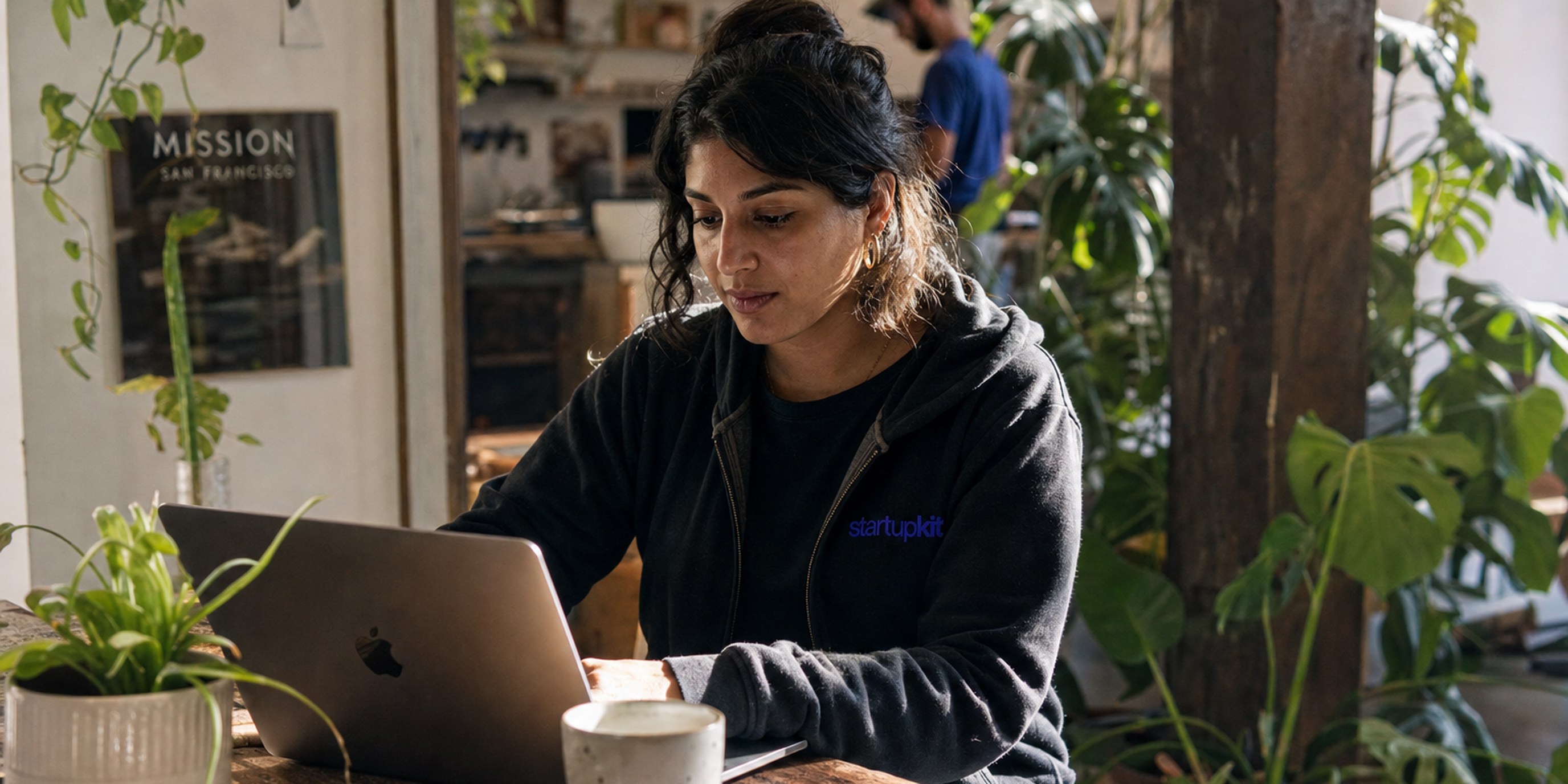 A startup founder reviewing her company's own branded careers page and candidate stage timeline on her laptop in a plant-filled studio, morning light through the window